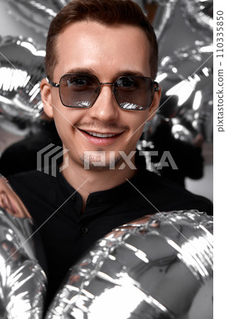 portrait of happy man in black shirt and sunglasses with a lot of silver air balloons background. birthday party 110335850