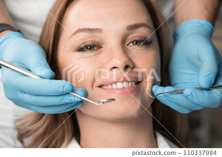 The dentist, holding the instruments, confidently and carefully treats the patient, providing a painless and professional approach. Woman smiling with white teeth charming smile close-up 110337984