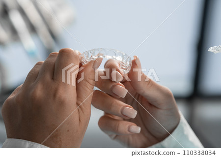 The dentist carefully holds the mouth guard in his hands, preparing for the procedure and demonstrating his adaptability to the highest standards of dental practice. The dentist carefully holds the mouth guard in his hands, preparing for the procedure and demonstrating his adaptability to the highest standards of dental practice. 110338034