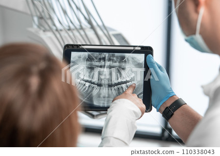 The dentist uses a tablet to visually explain the details of dental treatment so that the patient feels completely confident in her choice. Demonstrates a CT scan, an X-ray photograph 110338043