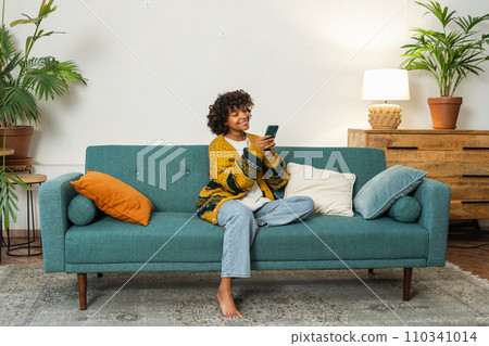 African girl holding smartphone touch screen typing scroll page at home. Woman with cell phone surfing internet using social media apps playing game. Shopping online Internet news cellphone addiction 110341014