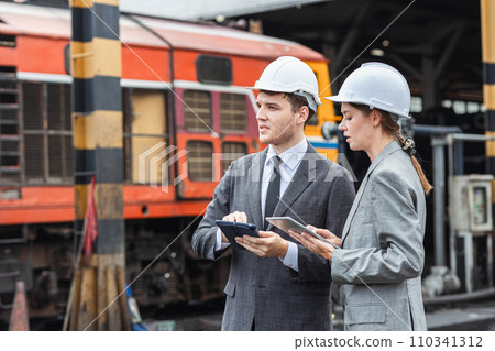 business man and woman standing together talking in heavy industry locomotive shop building site. 110341312