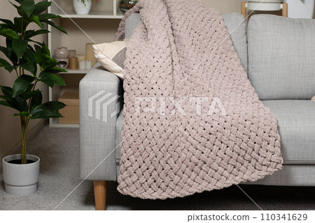 Knitted large plaid blanket in dusty rose light grayish-red color on the sofa. 110341629