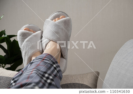 Stylish modern grey house slippers on women's feet lying on sofa 110341630