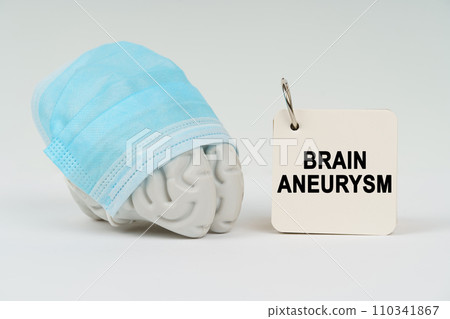 On a white surface next to the brain there is a notepad with the inscription - Brain aneurysm On a white surface next to the brain there is a notepad with the inscription - Brain aneurysm 110341867