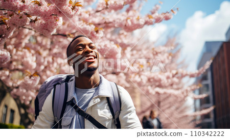 Modern happy young smiling dark-skinned African man against the backdrop of pink cherry blossoms and metropolis city. 110342222