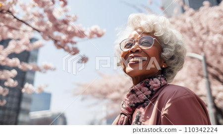 Modern happy elderly smiling dark-skinned African woman against the backdrop of pink cherry blossoms and metropolis city. 110342224