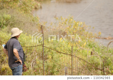 Birdwatcher and photographer by a lagoon. 110342365