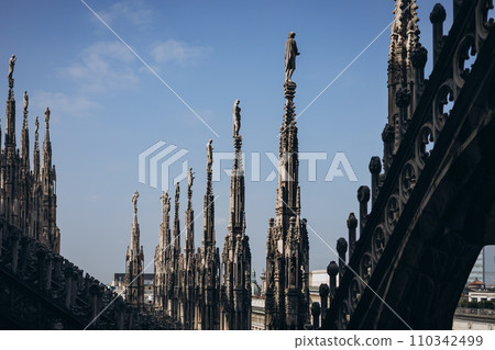 Roof of Milan Cathedral Duomo di Milano with Gothic spires and white marble statues. Top tourist attraction on piazza in Milan, Lombardia, Italy. Gothic architectural fragment Roof of Milan Cathedral Duomo di Milano with Gothic spires and white marble statues. Top tourist attraction on piazza in Milan, Lombardia, Italy. Gothic architectural fragment 110342499