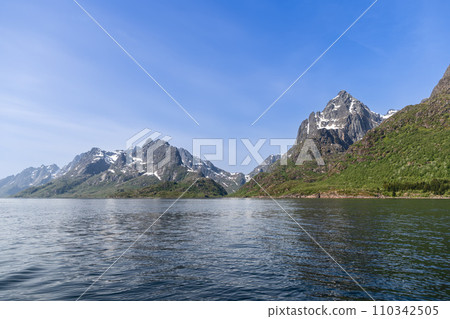 Snowy mountain crevices tower over a tranquil fjord in Lofoten, symbolizing Norway's serene grandeur Snowy mountain crevices tower over a tranquil fjord in Lofoten, symbolizing Norway's serene grandeur 110342505