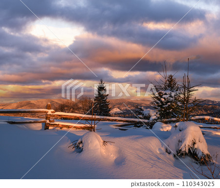Alpine village outskirts in last evening sunset sun light. Winter snowy hills and fir trees. Alpine village outskirts in last evening sunset sun light. Winter snowy hills and fir trees. 110343025