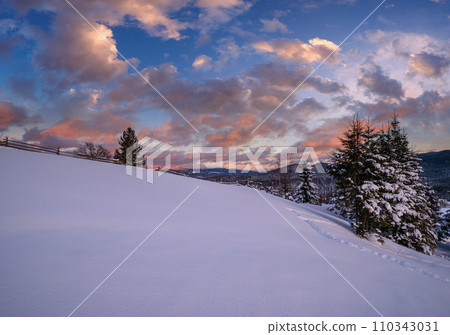 Alpine village outskirts in last evening sunset sun light. Winter snowy hills and fir trees. 110343031