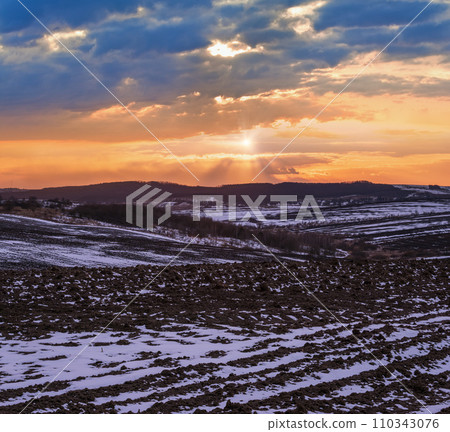 Black earth, arable land covered with the last snow, early spring. Calm evening sunset in the Ukrainian countryside, Lviv region. 110343076