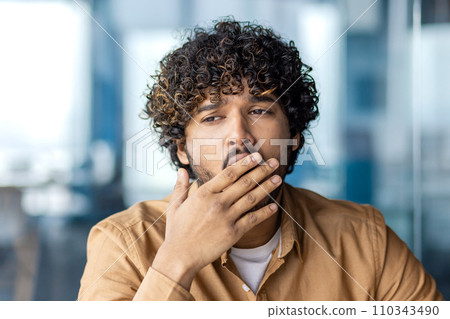 Young overworked and overtired businessman yawning, working inside office with laptop, boring long routine work, man in casual clothes. 110343490