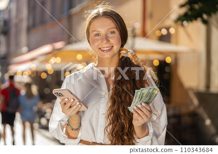 Happy teenager girl counting money dollar cash, use smartphone calculator app in urban city street Happy teenager girl counting money dollar cash, use smartphone calculator app in urban city street 110343684