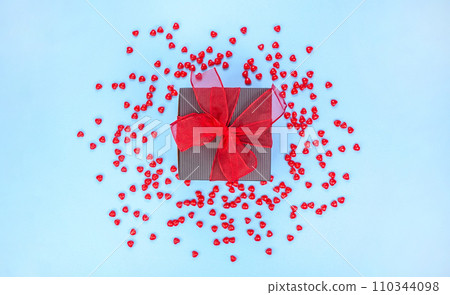 Gift box decorated with red ribbon bow on blue background with red candies. St. Valentine Day. Love, gift concept. Gift box decorated with red ribbon bow on blue background with red candies. St. Valentine Day. Love, gift concept. 110344098