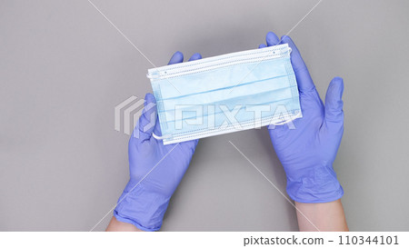 Hand in blue gloves of doctor or nurse holding protective blue face mask over grey background with copy space. New vaccine. Unknown vaccine. Medical gloves. Hand in blue gloves of doctor or nurse holding protective blue face mask over grey background with copy space. New vaccine. Unknown vaccine. Medical gloves. 110344101
