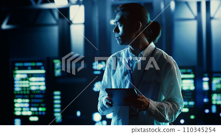Asian employee walking through data center equipment clusters providing processing resources for different workloads. Productive engineer examining server rigs tasked with solving complex operations Asian employee walking through data center equipment clusters providing processing resources for different workloads. Productive engineer examining server rigs tasked with solving complex operations 110345254