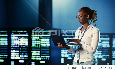 Computer scientist programming in server farm housing advanced equipment storing massive datasets. Developer running code on laptop to fix data center racks doing complex computational operations 110345255