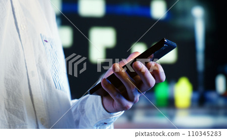 Man walking around city at night, scrolling on mobile phone, blurry urban background with bokeh lights. Person using smartphone while strolling on streets illuminated by lamps, extreme close up 110345283