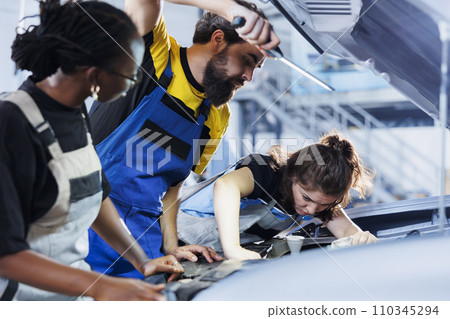 Team of technicians in auto repair shop working together on fixing car, discussing best options. Diverse employees collaborating on servicing broken vehicle, checking for fuel tank 110345294