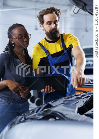 Mechanic in car service uses laptop to calculate invoice after fixing broken automobile distributor. Certified auto repair shop worker uses device to inform woman of final costs after mending vehicle 110345297