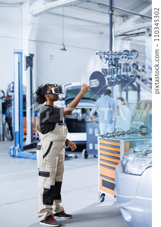 Qualified engineer in repair shop using VR googles and augmented reality hologram to visualize car parts in order to fix them. BIPOC woman using AR technology while working on damaged vehicle motor 110345302