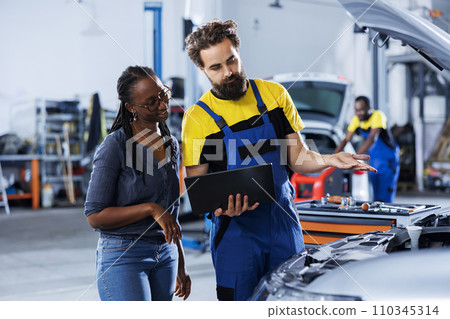Mechanic at auto repair shop conducts annual vehicle checkup, informing customer about needed radiator replacement. Knowledgeable garage worker talks with customer after finishing car inspection Mechanic at auto repair shop conducts annual vehicle checkup, informing customer about needed radiator replacement. Knowledgeable garage worker talks with customer after finishing car inspection 110345314