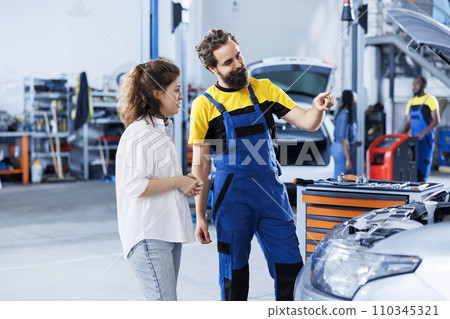 Technician in repair shop using augmented reality holograms to show customer car performance parameters. Trained garage employee using futuristic vr headset to examine damaged exhaust pipes 110345321