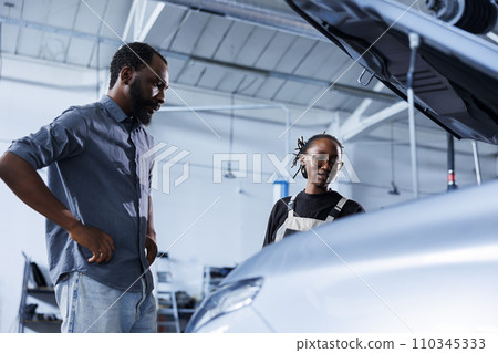 Mechanic at auto repair shop conducts annual vehicle checkup, informing customer about needed steering mechanism replacement. Competent garage worker talks with customer after finishing car inspection Mechanic at auto repair shop conducts annual vehicle checkup, informing customer about needed steering mechanism replacement. Competent garage worker talks with customer after finishing car inspection 110345333