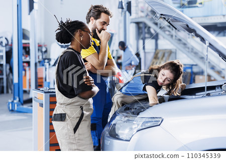Team of mechanics in auto repair shop working together on fixing car, discussing best options. Multiethnic employees collaborating on servicing broken vehicle, checking for fuel tank Team of mechanics in auto repair shop working together on fixing car, discussing best options. Multiethnic employees collaborating on servicing broken vehicle, checking for fuel tank 110345339