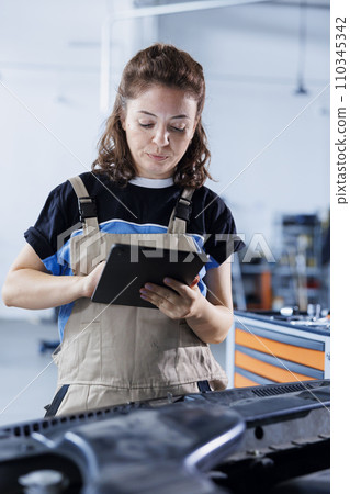 Diligent serviceman in car service orders new engine for damaged vehicle using tablet. Expert looking online for components to replace old ones in malfunctioning automobile Diligent serviceman in car service orders new engine for damaged vehicle using tablet. Expert looking online for components to replace old ones in malfunctioning automobile 110345342