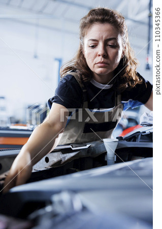 Licensed mechanic in garage finishing repairing car, looking underneath vehicle hood to remove remaining oil leaks. Employee does routine emissions cleaning on client automobile in auto repair shop 110345366