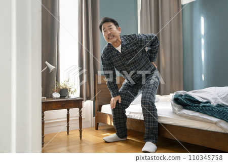 Image of a man in his mid-50s in pajamas with back pain and strained back Image of a man in his mid-50s in pajamas with back pain and strained back 110345758