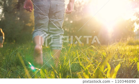 Little contented child joyfully dashes barefoot on grass in park in warm weather Little contented child joyfully dashes barefoot on grass in park in warm weather 110346890
