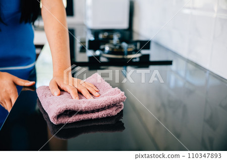 A cheerful housewife ensures safety and hygiene by wiping her kitchen table with a rag and detergent. Illustrating routine cleaning and care for a sanitized living space. Wiping cloth kitchen 110347893