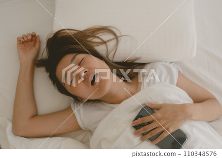 Funny Asian woman falls asleep with her mobile phone next to her 110348576
