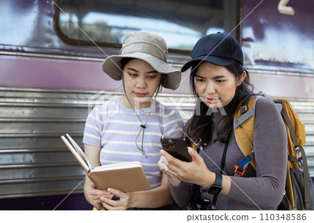 two women traveler friends are at the train station checking the map of the city on mobile 110348586