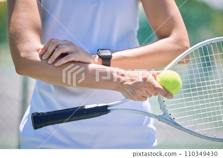 Sports, arm pain and tennis player with a racket and ball standing on a court during for a match. Closeup of a health, strong and professional athlete with equipment touching a medical elbow injury. 110349430