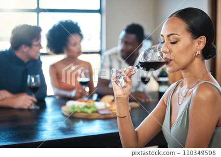 A woman drinking a glass of wine at a dinner table with friends in a restaurant and enjoying the luxury alcohol. Young African American female having fun dining with people at a celebration A woman drinking a glass of wine at a dinner table with friends in a restaurant and enjoying the luxury alcohol. Young African American female having fun dining with people at a celebration 110349508