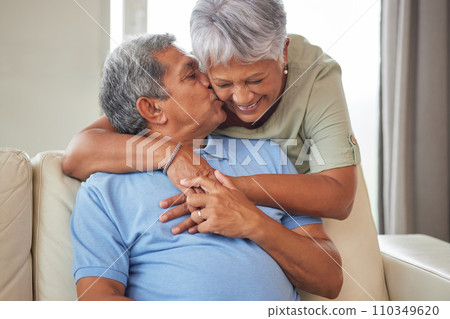 Happy senior couple kiss, hug and smile with love while relax on the sofa in the living room at home. Playful, fun man and woman laughing, smiling and enjoying retirement life together in their house 110349620