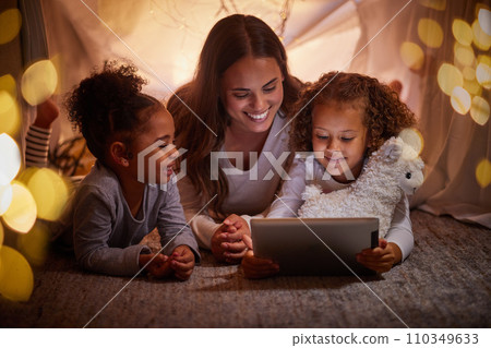 Mother and children live streaming on an app using a tablet in a tent camping at home at night. Happy mom and kids watching online content or playing games with house wifi in the dark or evening 110349633