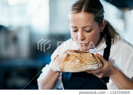 Baker, pastry chef and cafe owner smelling a loaf of fresh baked bread in the kitchen of her coffee shop. Closeup of a female cook enjoying the aroma of a freshly made dough treat or consumables 110350089