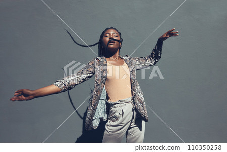Fashion, style and trendy black woman against a gray background wall in a city, town and downtown. Street beauty model with funky, cool and hipster hair in edgy motion or movement expression outdoors Fashion, style and trendy black woman against a gray background wall in a city, town and downtown. Street beauty model with funky, cool and hipster hair in edgy motion or movement expression outdoors 110350258