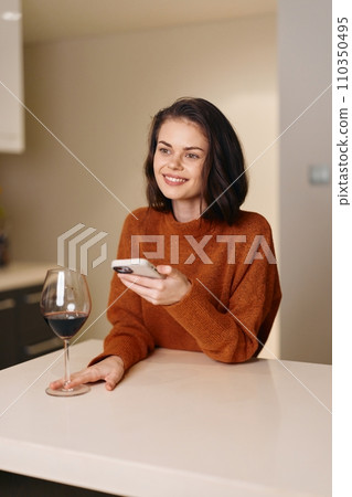 Relaxed Female Sitting at Home, Enjoying Wine and Using Smartphone 110350495