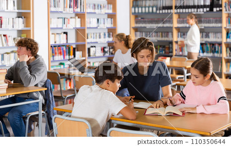 Group of schoolchildren reading books together in library and preparing for school exam Group of schoolchildren reading books together in library and preparing for school exam 110350644