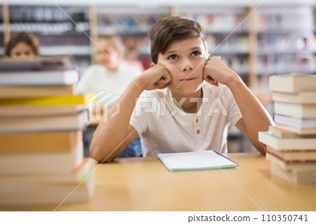 Bored teenage boy trying to prepare for exam in library 110350741