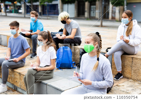 Focused teen students in masks during lesson outside 110350754
