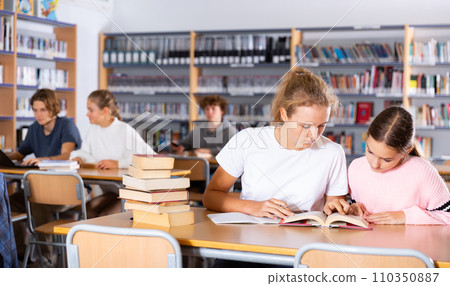 Two female friends reading books together and preparing for exams in school library Two female friends reading books together and preparing for exams in school library 110350887