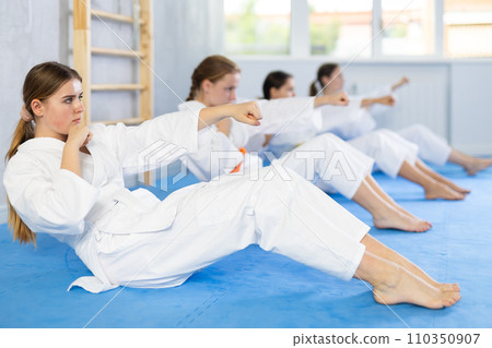 Team of teenage girls in kimono train abdominal muscles and do punches at the same time during karate or judo training 110350907